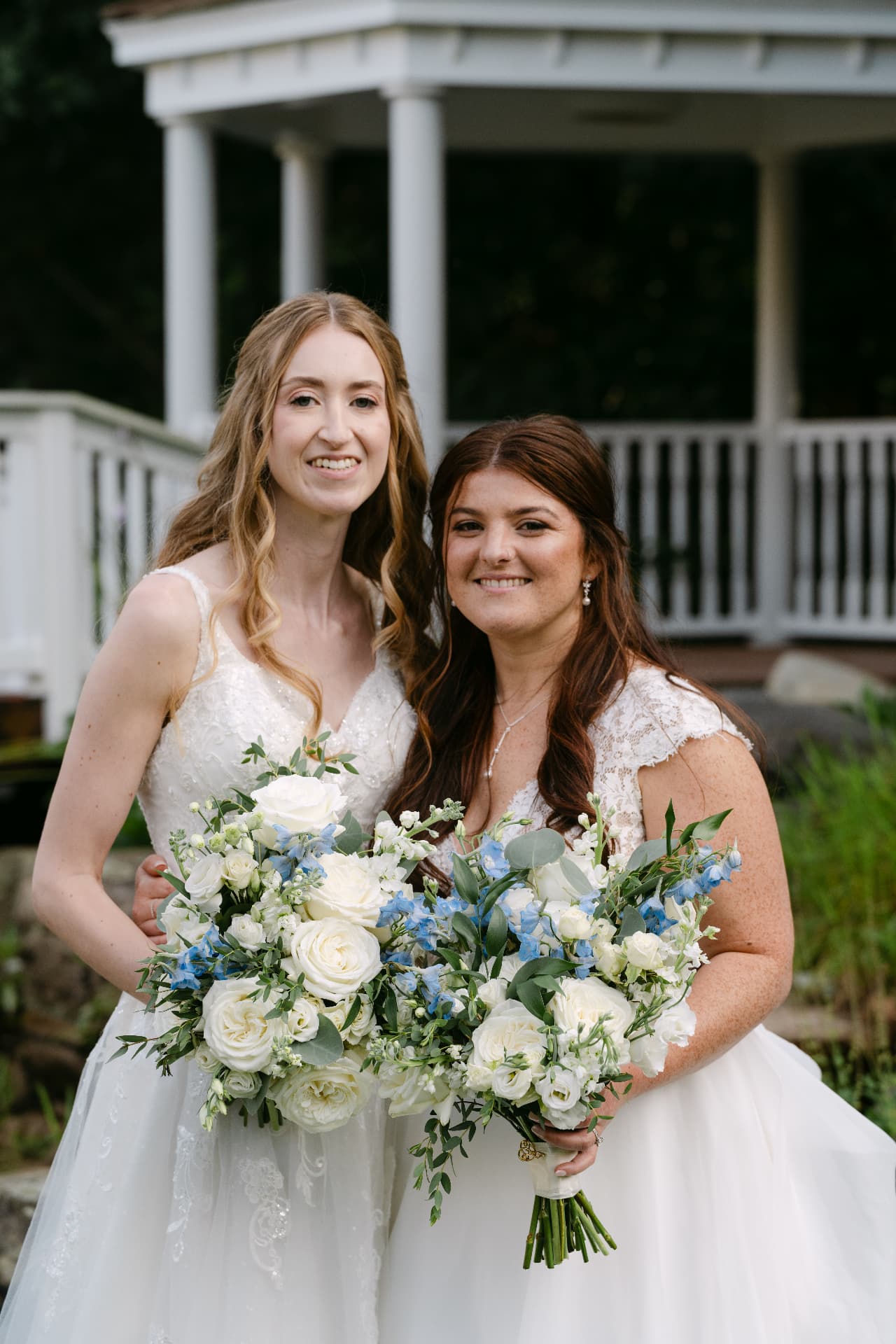Two brides with white and blue bouquets in front of a gazebo