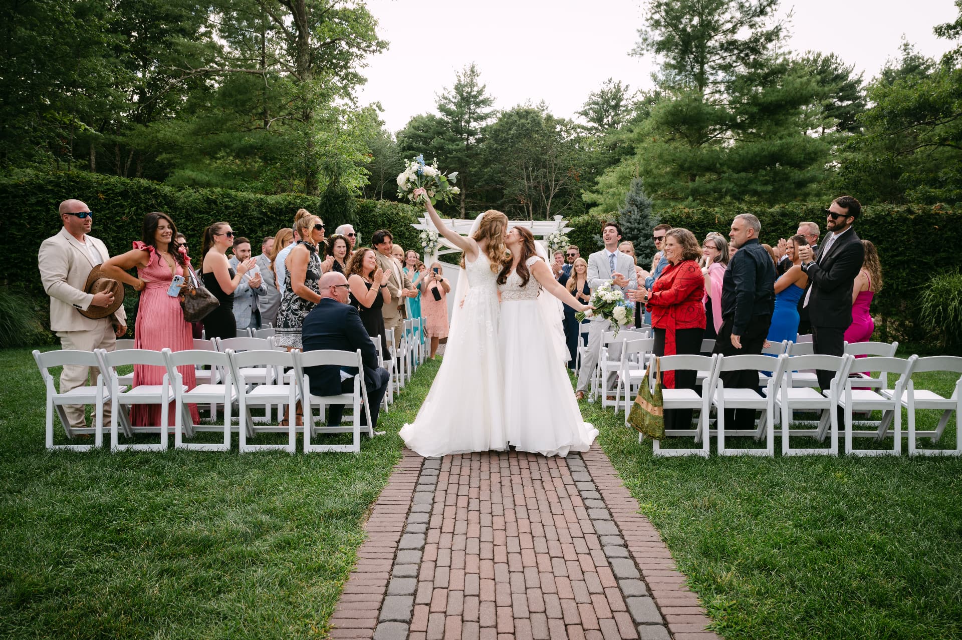 Brides kissing during their recessional as guests cheer